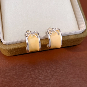 Detail of silver C-shaped bow earrings with yellow enamel on a velvet jewelry box
