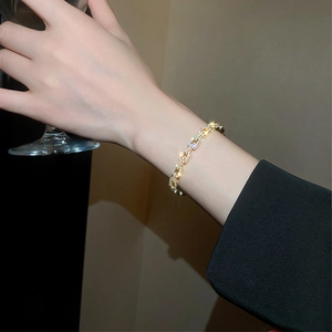 Detailed view of a gold-plated zircon chain bracelet worn while holding a glass cup