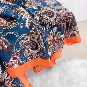 Large dark blue paisley print silk scarf with orange borders on white carpet background