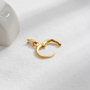 Detailed macro view of a single gold cartilage hoop with a clear rectangular gemstone charm