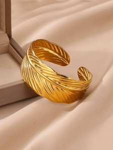 Détail du bracelet ouvert doré en forme de plume avec relief sur satin de couleur champagne
