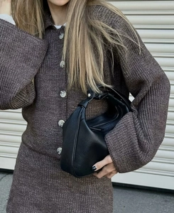 Gros plan du sac hobo en cuir grainé noir porté avec un ensemble en maille marron