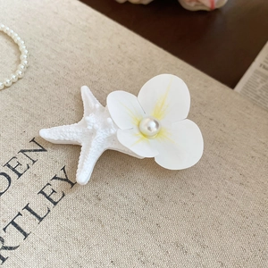 Detailed close-up of a white starfish and fabric flower hair clip with a pearl center