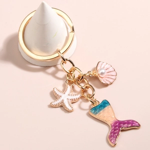 Golden mermaid tail keychain with pink shell and white starfish charm on beige background