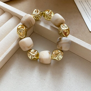 Detail of irregular gold beads and cream resin marble beads on a stretch bracelet