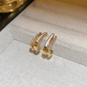 Macro shot of double-layered C-shaped gold earrings with white inlay and pavé zircon stones