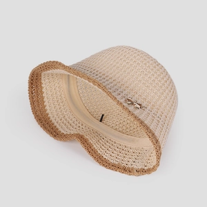 Close-up of beige knit bucket hat with breathable mesh and golden bow charm detail