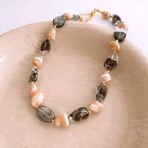 Gros plan d'un collier de perles irrégulières abricot et noires sur assiette