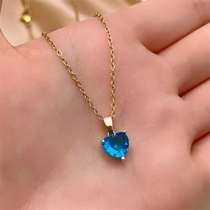 Close-up of heart-shaped dark blue zircon pendant on a gold chain held in palm
