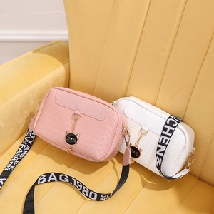 Pink and white woven camera bags with cat charms and wide straps on a yellow velvet chair
