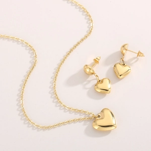 Detailansicht des herzförmigen Goldschmucksets mit Halskette und Ohrringen auf Beige