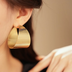 Close-up of a model wearing wide gold earrings with fine parallel textured lines