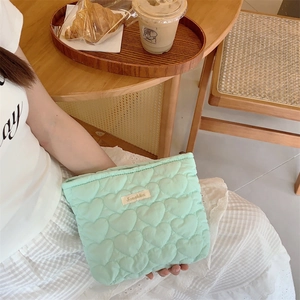 Close-up of a light green quilted heart pouch held by a woman in a cozy cafe setting