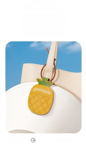 Macro view of pineapple-shaped magnetic hat clip attached to a beige bag and sun hat
