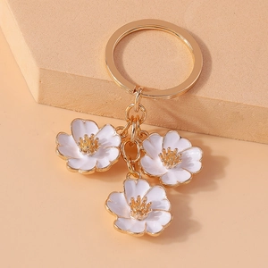 Detail of a golden metal keychain with three white peach blossom flower charms