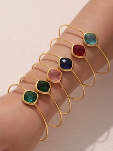 Close-up of six gold-plated open bangles featuring square-cut colorful faceted gemstones