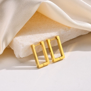 Macro shot of rectangular gold-plated stainless steel earrings on marble and silk fabric