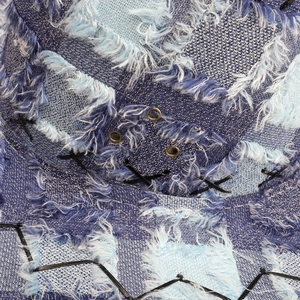 Macro detail of frayed blue denim patchwork with bronze eyelets and contrast stitching