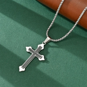 Detail of silver cross pendant with black inlay and box chain on textured green surface
