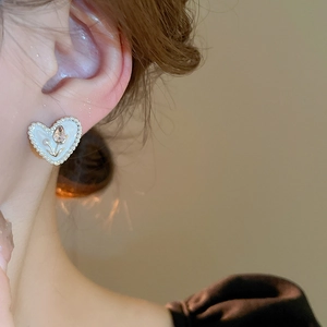 Close-up of heart earring with cream pearl trim and golden tulip relief on model