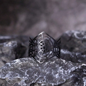 Detailed close-up of matte black spider web cuff bracelet on dark stone surface