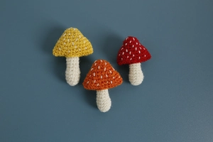 Top view of three handmade crochet mushroom brooches in yellow orange and red wool