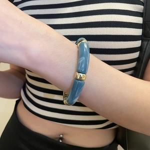 Détail d'un bracelet en acrylique marbré bleu-gris avec des accents en métal doré poli