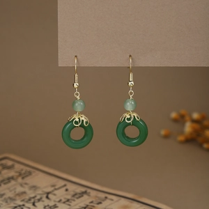 Detail of green jade-style drop earrings with gold hooks and tassels on vintage book background