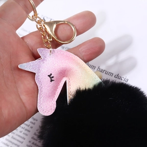 Detalle macro del dije de unicornio con purpurina, pompón negro y clip de llavero dorado