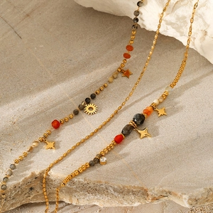 Macro detail of layered gold stainless steel necklace with natural stones and star pendants