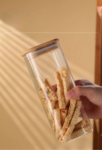 Close-up of airtight glass storage jar with bamboo lid held by hand in a kitchen setting