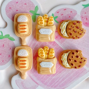 Macro shot of 6 miniature resin food charms including bread trays and bitten cookies