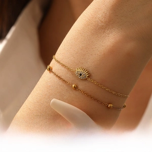 Detailed close-up of double-layered gold chain bracelet with sparkling evil eye pendant