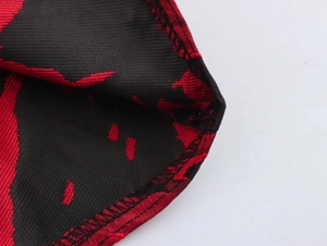 Close-up of black and red jacquard fabric with detailed overlock stitching on the hemline