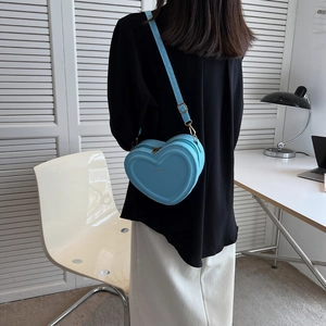 Borsa a tracolla blu a forma di cuore indossata da una modella in un ufficio moderno