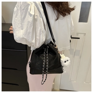 Detail of black leather bucket bag with silver chains and plush pendant on model