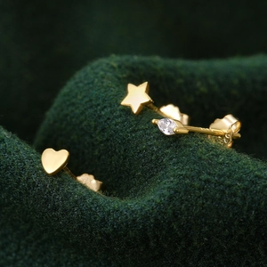 Macro shot of three gold S925 silver stud earrings with heart, star and zircon on green fabric