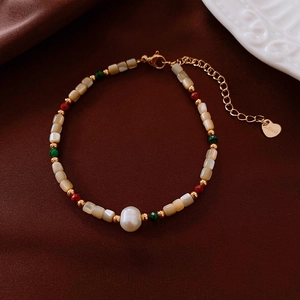Macro detail of 18k gold-plated heart charm and freshwater pearls on stainless steel bracelet