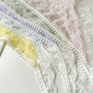 Detailed view of colorful pleated headscarves with white lace trim and pom-pom edges