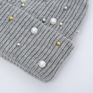 Detailed macro view of gray cable knit beanie featuring decorative white pearls and metal beads