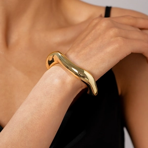 Bracciale rigido dorato ondulato lucido con finitura a specchio su polso donna