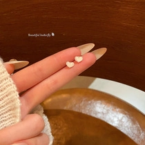 Close-up of minimalist cream heart stud earrings held between fingers for size detail