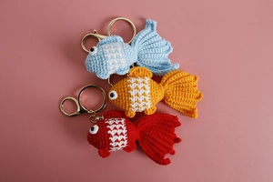 Top view of three handmade crochet goldfish keychains in blue, orange, and red colors
