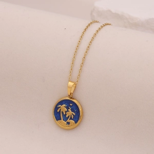 Golden coconut tree pendant necklace with blue enamel on a minimalist white background
