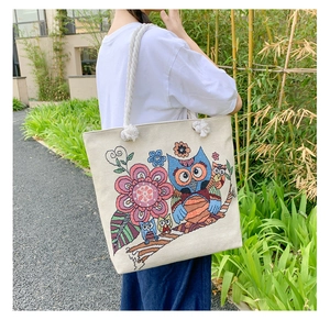 Close-up of beige canvas tote bag with colorful owl and floral embroidery detail