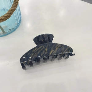 Detail of large acetate hair claw clip featuring elegant gold streamline feather patterns