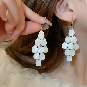 Detailed view of elegant white tiered teardrop shell earrings worn by a model