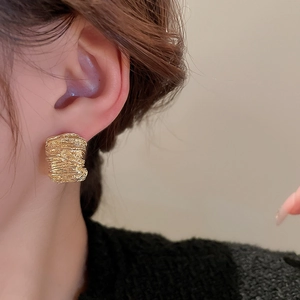 Close-up of golden irregular textured earrings worn on ear with metallic details
