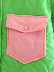 Dettaglio giacca trapuntata verde neon con tasca a contrasto rosa e bottone a pressione