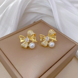 Macro detail of golden bow earrings with heart zircon and elegant white pearl drop